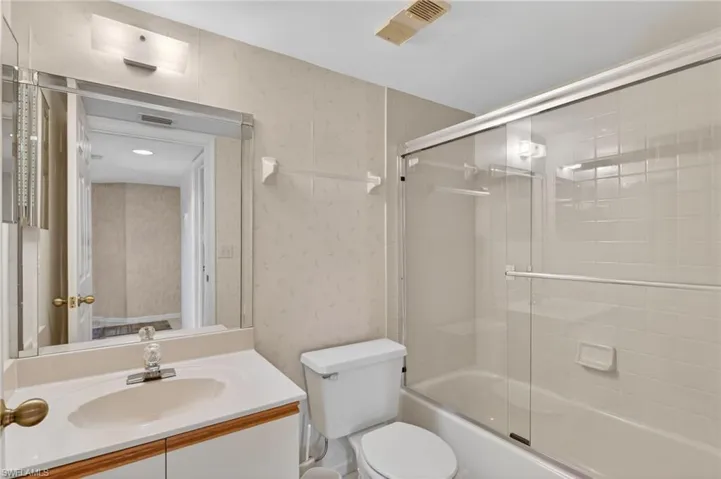 Full bath with vanity, enclosed tub / shower combo, and wallpapered walls
