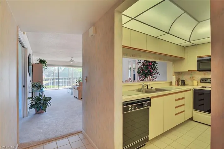 Kitchen featuring light carpet, black appliances, light countertops, light tile patterned floors, and tasteful backsplash