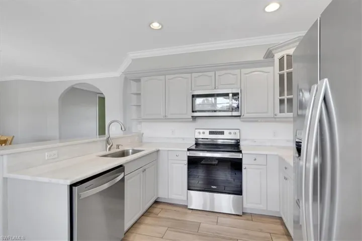 Kitchen with appliances with stainless steel finishes, ornamental molding, open shelves, wood finish floors, and recessed lighting