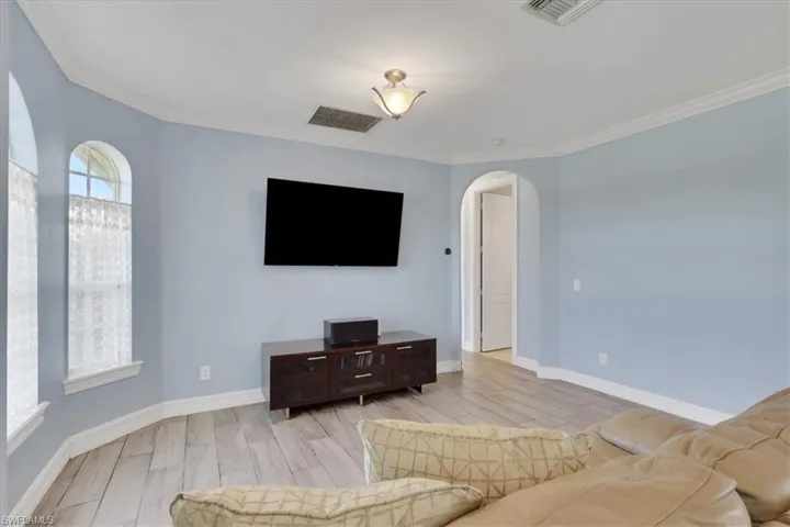 Living area featuring arched walkways, wood finish floors, and crown molding