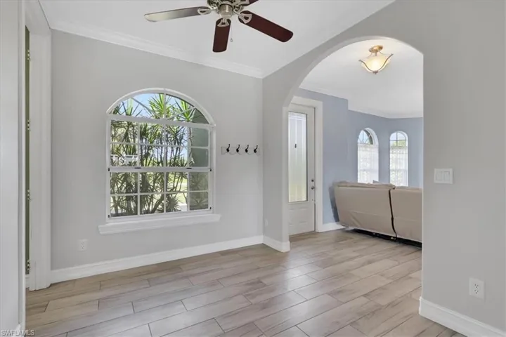 Foyer entrance with ornamental molding, wood tiled floors, arched walkways, and ceiling fan