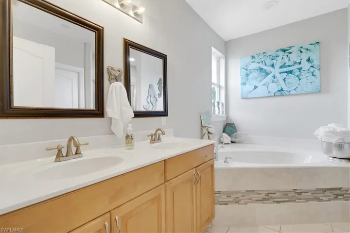 Full bath with double vanity, a garden tub, and light tile patterned flooring