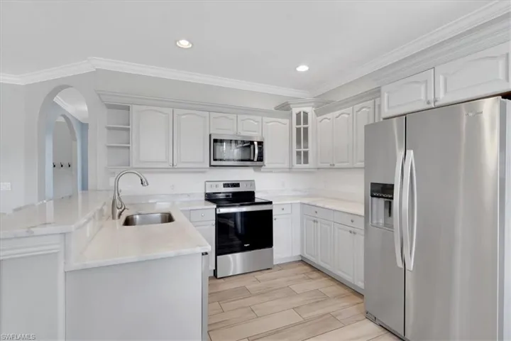 Kitchen with appliances with stainless steel finishes, ornamental molding, open shelves, wood finish floors, and glass insert cabinets