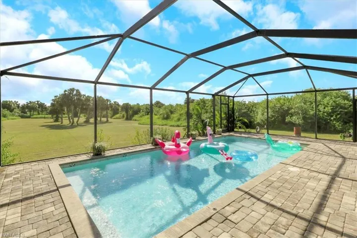 Outdoor pool featuring a sunroom, glass enclosure, a yard, and a patio area