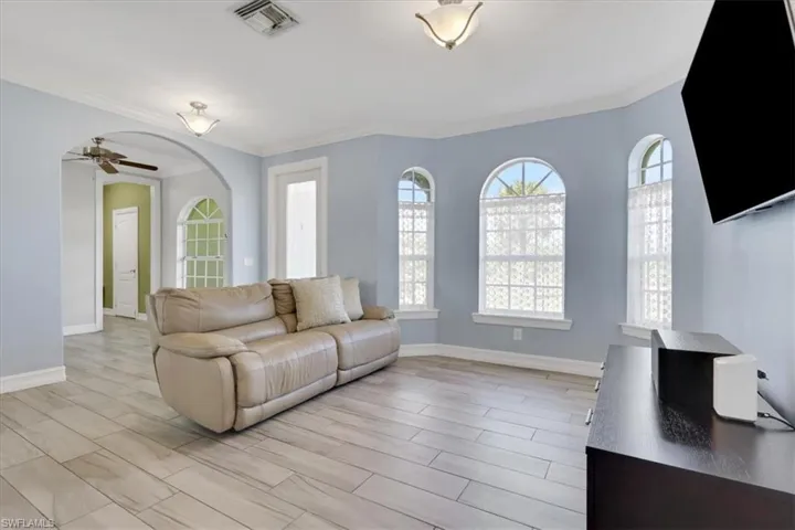 Living room with crown molding, wood tiled floors, ceiling fan, and arched walkways