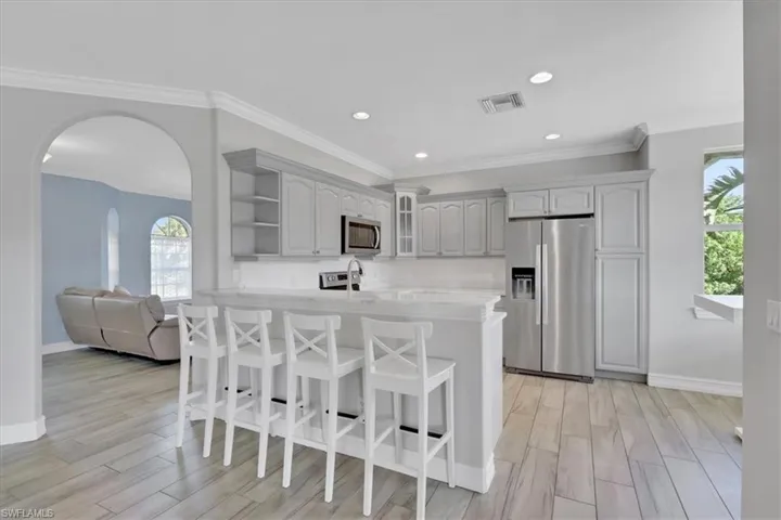 Kitchen with a breakfast bar area, appliances with stainless steel finishes, arched walkways, open shelves, and wood finish floors