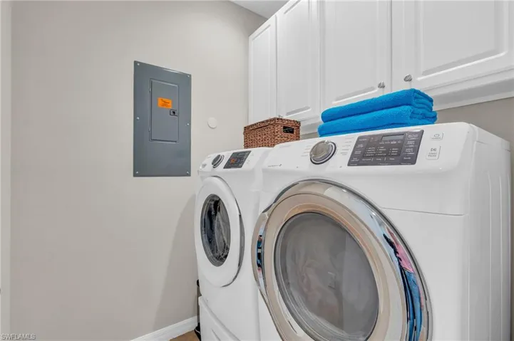 Laundry room featuring electric panel, washer and clothes dryer, and cabinets
