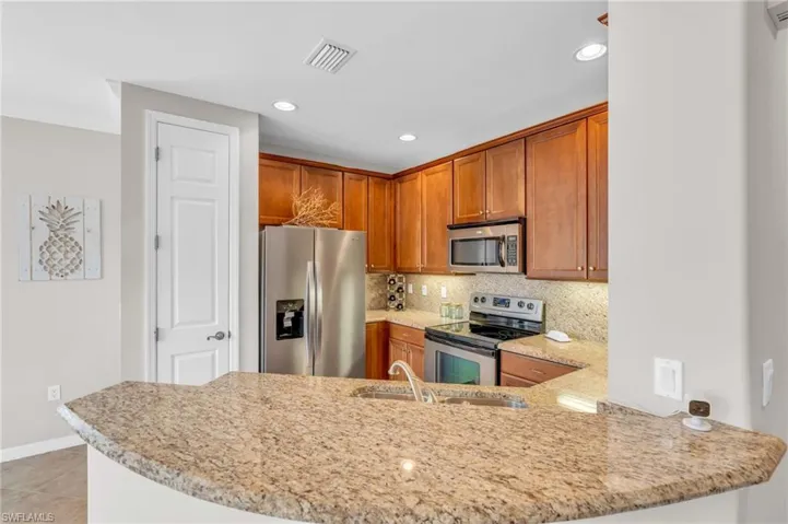 Kitchen featuring kitchen peninsula, decorative backsplash, light stone countertops, stainless steel appliances, and sink