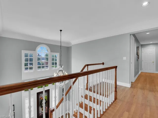 Hall with light wood-type flooring, crown molding, and a notable chandelier