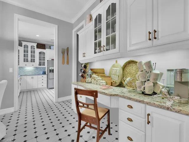 Kitchen featuring built in desk, stainless steel fridge, white cabinetry, and ornamental molding