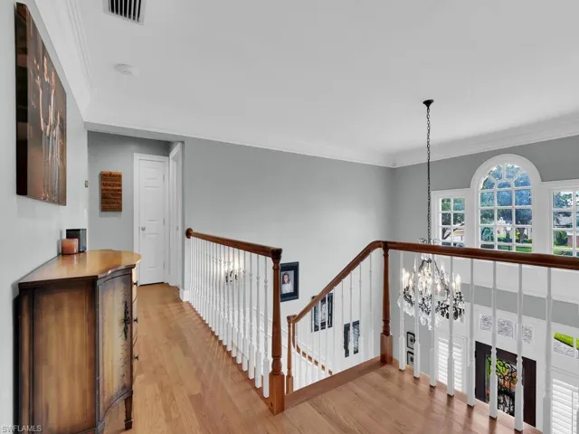 Hall with crown molding, a notable chandelier, and light hardwood / wood-style floors