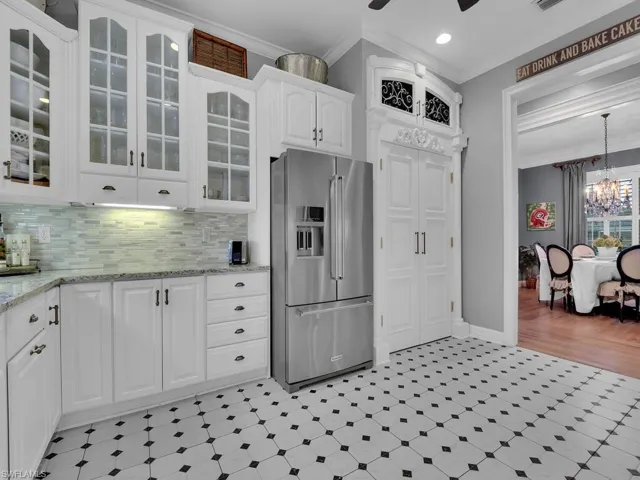 Kitchen featuring ceiling fan with notable chandelier, pendant lighting, high end refrigerator, ornamental molding, and white cabinetry