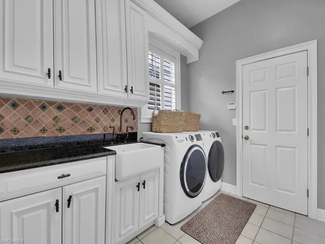 Laundry area with washing machine and clothes dryer, cabinets, sink, and light tile patterned flooring