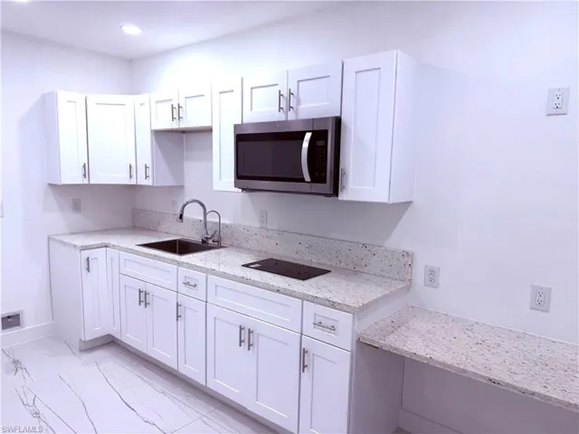 Kitchen with stainless steel microwave, white cabinetry, light stone counters, and light marble finish floors
