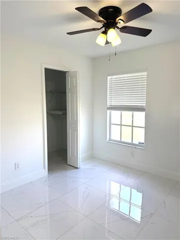 Unfurnished bedroom featuring light marble finish floors, a walk in closet, and a ceiling fan