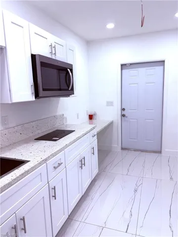 Kitchen with stainless steel microwave, light marble finish floors, white cabinets, light stone countertops, and recessed lighting