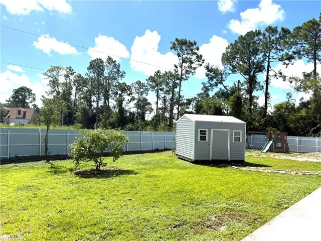 Fenced backyard featuring a playground and a storage unit