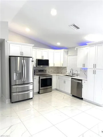 Kitchen with appliances with stainless steel finishes, vaulted ceiling, white cabinetry, tasteful backsplash, and light countertops