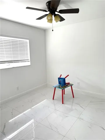 Empty room featuring light marble finish flooring and ceiling fan