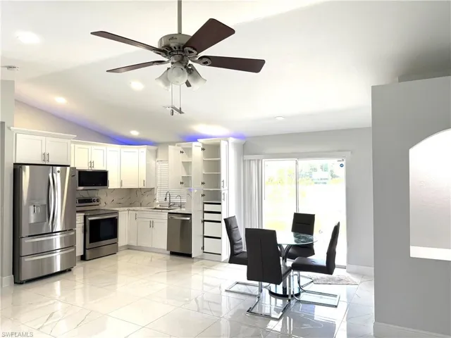 Kitchen with appliances with stainless steel finishes, vaulted ceiling, backsplash, white cabinets, and ceiling fan