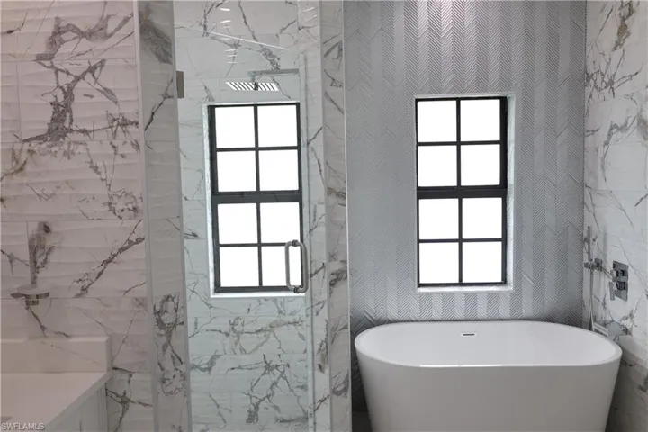 Bathroom featuring a marble finish shower, marble tiled floors, a freestanding bath, and vanity