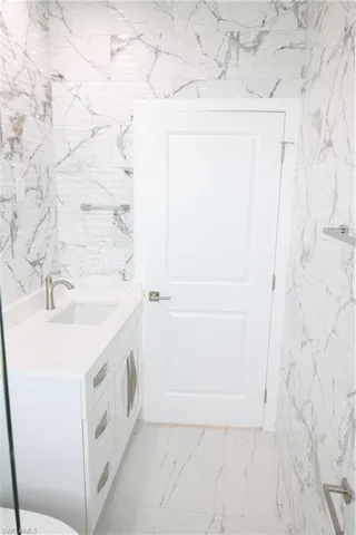 Half bath featuring vanity, marble finish flooring, and tile walls