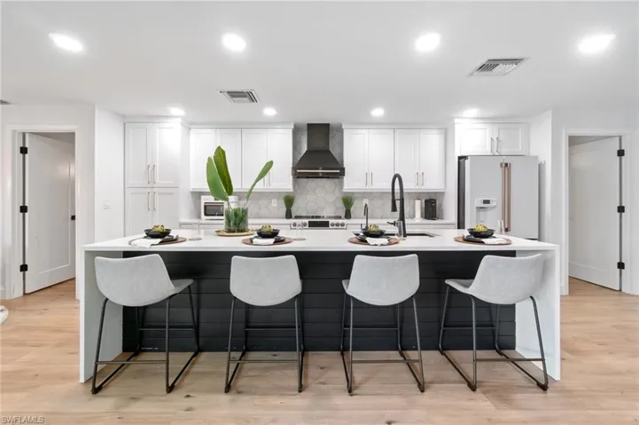 Kitchen featuring white cabinets, light hardwood / wood-style floors, white appliances, and wall chimney range hood