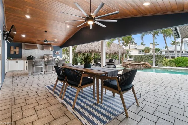 View of shaded rear patio featuring a rich wood plank vaulted ceiling, outdoor kitchen, outdoor bar, and modern ceiling fans