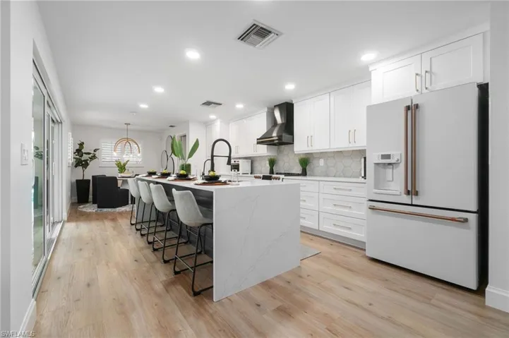 Kitchen with wall chimney range hood, light hardwood / wood-style floors, high end white fridge, a kitchen island with sink, and white cabinets