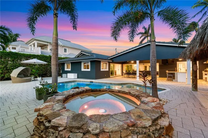 Pool at dusk with an in ground hot tub, an outdoor bar, a patio area, and exterior kitchen