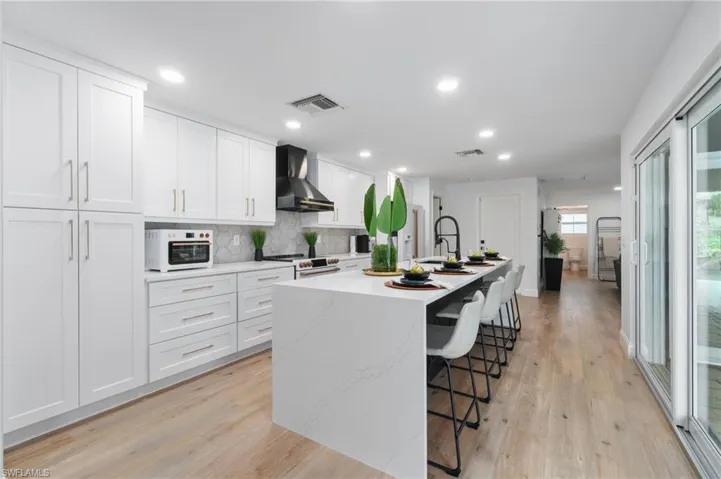 Kitchen with a kitchen island with sink, a kitchen breakfast bar, wall chimney range hood, light hardwood / wood-style floors, and white cabinetry