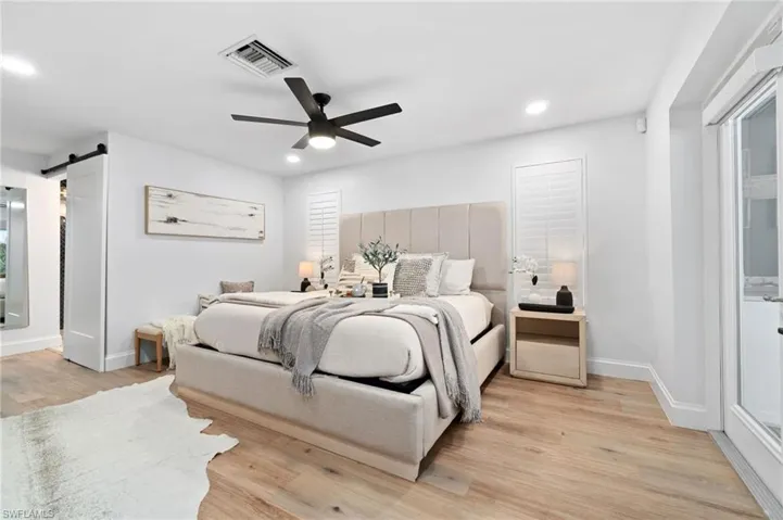 Primary Bedroom en-suite featuring a barn bathroom door, new modern ceiling fan, and light wood look white oak LVP style flooring.