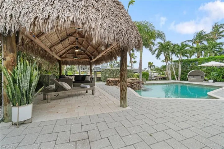 View of swimming pool with a large custom chickee hut, a roof covered entertaining/cooking outdoor living space, and a large pool/spa patio area.