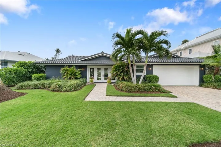 View of front of house with lush, tropical landscaping & green space in the front yard, double french door entry and a 2 car epoxy floor and storage system garage.