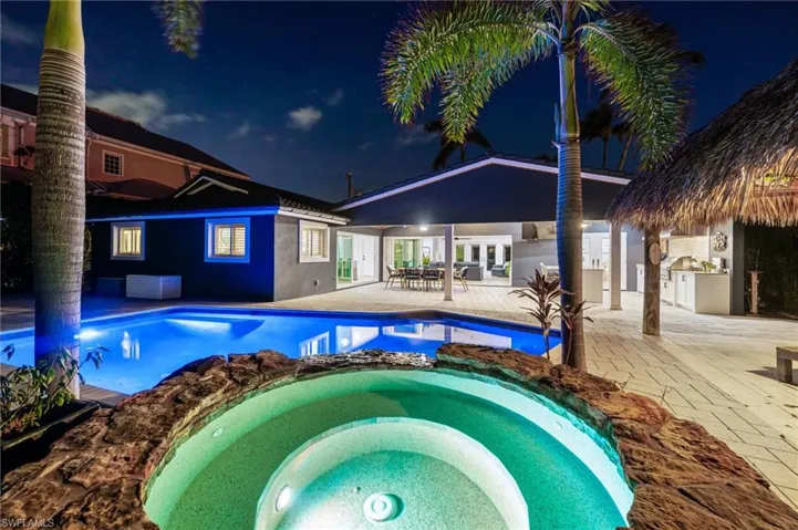 Pool at night with a patio area, an in ground hot tub, and an outdoor kitchen