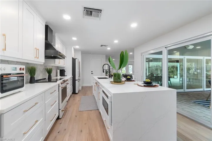 Kitchen featuring white cabinetry, a kitchen island with sink, wall chimney range hood, and appliances with stainless steel finishes