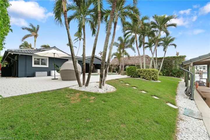 View of back yard near seawall featuring a swimming pool/spa, chicken hut, covered dining and outdoor kitchen and expansive paver patio space for entertaining!  , Greenspace and seawall leading out to a dock/boathouse.