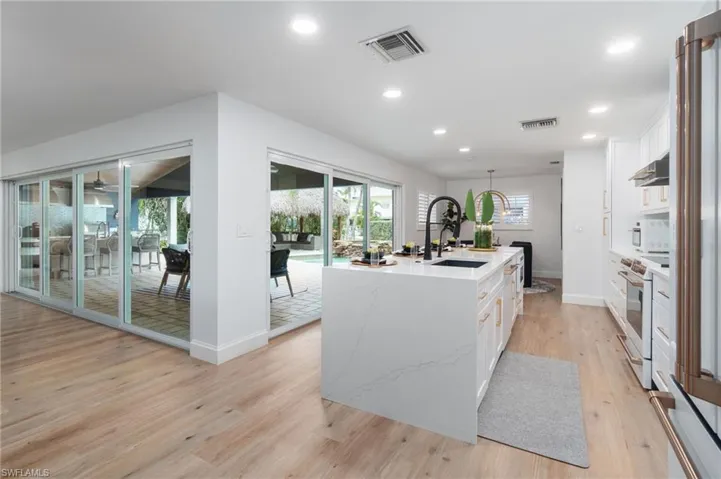 Kitchen with white cabinetry, sink, white appliances, a kitchen island with sink, and light wood-type flooring
