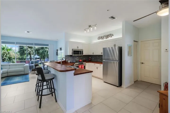 Kitchen with a kitchen breakfast bar, kitchen peninsula, stainless steel appliances, white cabinets, and butcher block countertops