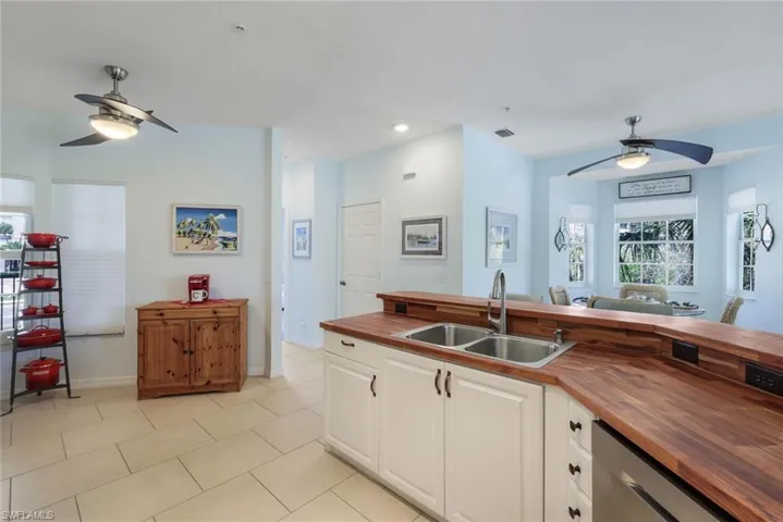 Kitchen with light tile patterned floors, white cabinetry, dishwasher, butcher block counters, and sink