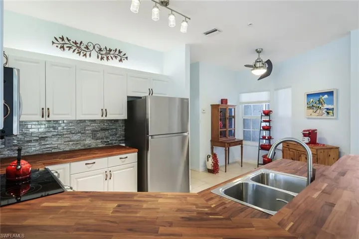 Kitchen with wooden counters, decorative backsplash, sink, white cabinets, and appliances with stainless steel finishes