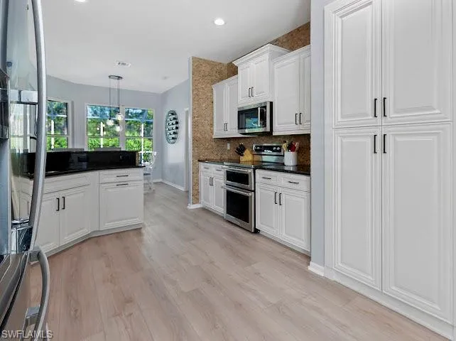 Kitchen with decorative backsplash, appliances with stainless steel finishes, white cabinetry, hanging light fixtures, and recessed lighting