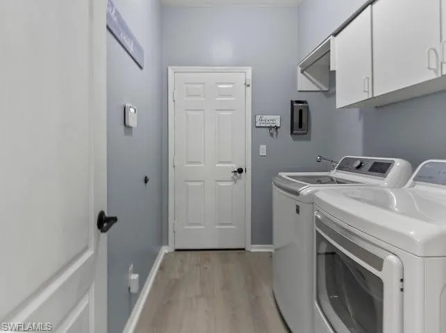 Laundry area with cabinet space, light wood-style floors, and separate washer and dryer