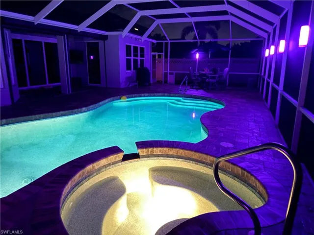 View of pool with custom lights, a pool with connected hot tub, a lanai, and a patio