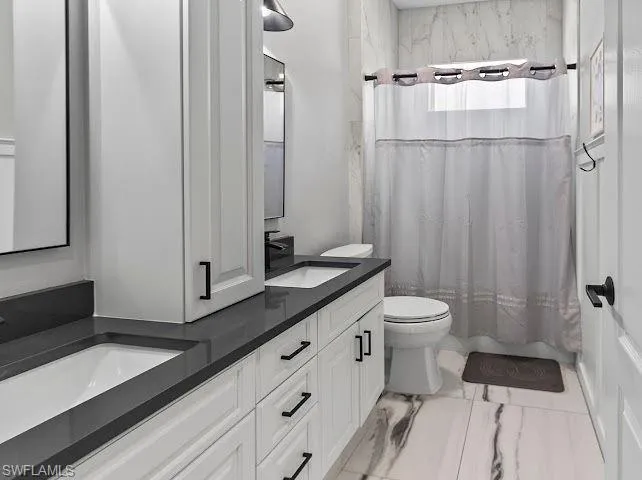 Full bathroom featuring double vanity, shower / tub combo, and light marble finish flooring