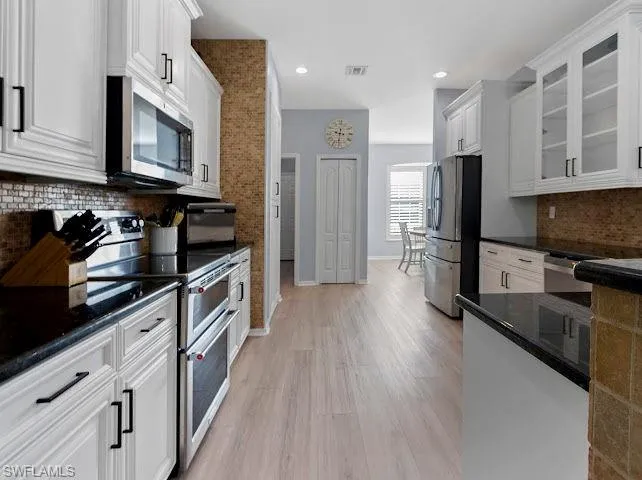 Kitchen with backsplash, appliances with stainless steel finishes, white cabinets, light wood finished floors, and recessed lighting