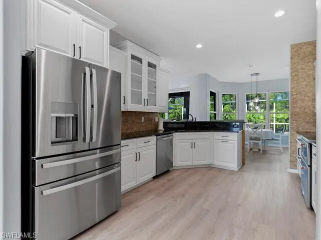 Kitchen with appliances with stainless steel finishes, glass insert cabinets, pendant lighting, white cabinetry, and recessed lighting