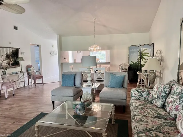 Living room with ceiling fan with notable chandelier, high vaulted ceiling, and wood-style laminate flooring