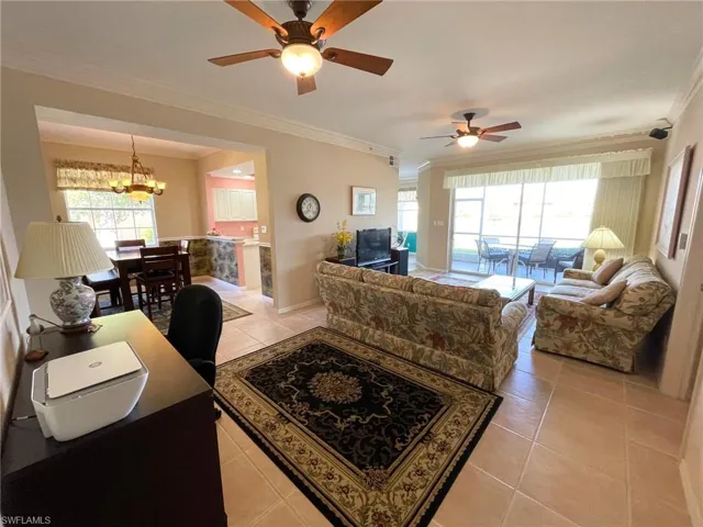Living room with ceiling fan with notable chandelier, ornamental molding, and light tile patterned flooring
