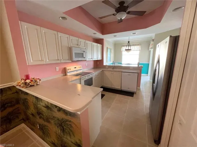 Kitchen with pendant lighting, white appliances, a tray ceiling, light tile patterned flooring, and kitchen peninsula